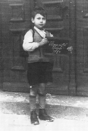 Das Foto von 1934 zeigt Wolfgang Brühl mit Schiefertafel vor einer großen Schultür.